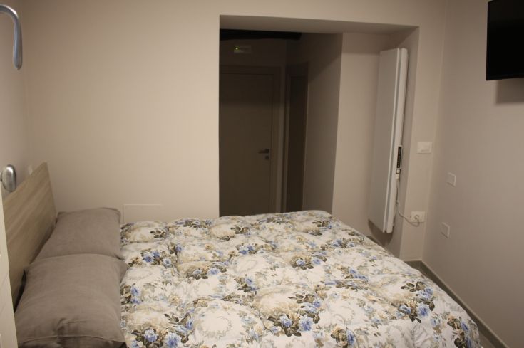 Camera matrimoniale semplice con letto in tessuto fiorato e elementi di arredo contemporanei.