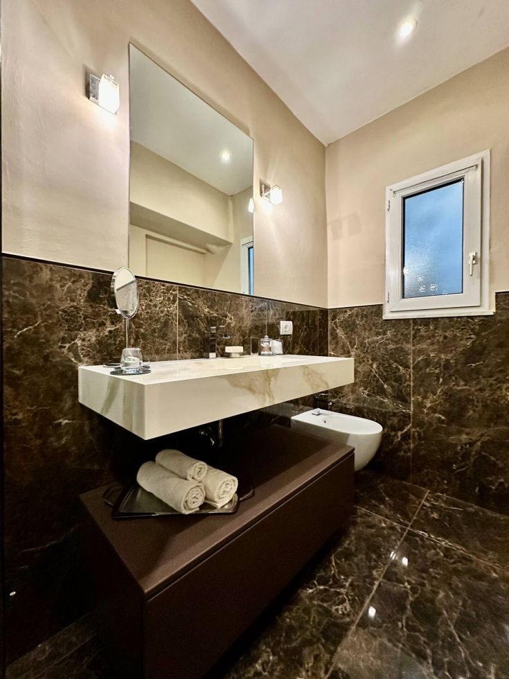 Bagno con lavabo sospeso, specchio e piastrelle in marmo scuro. Ambiente semplice e curato.