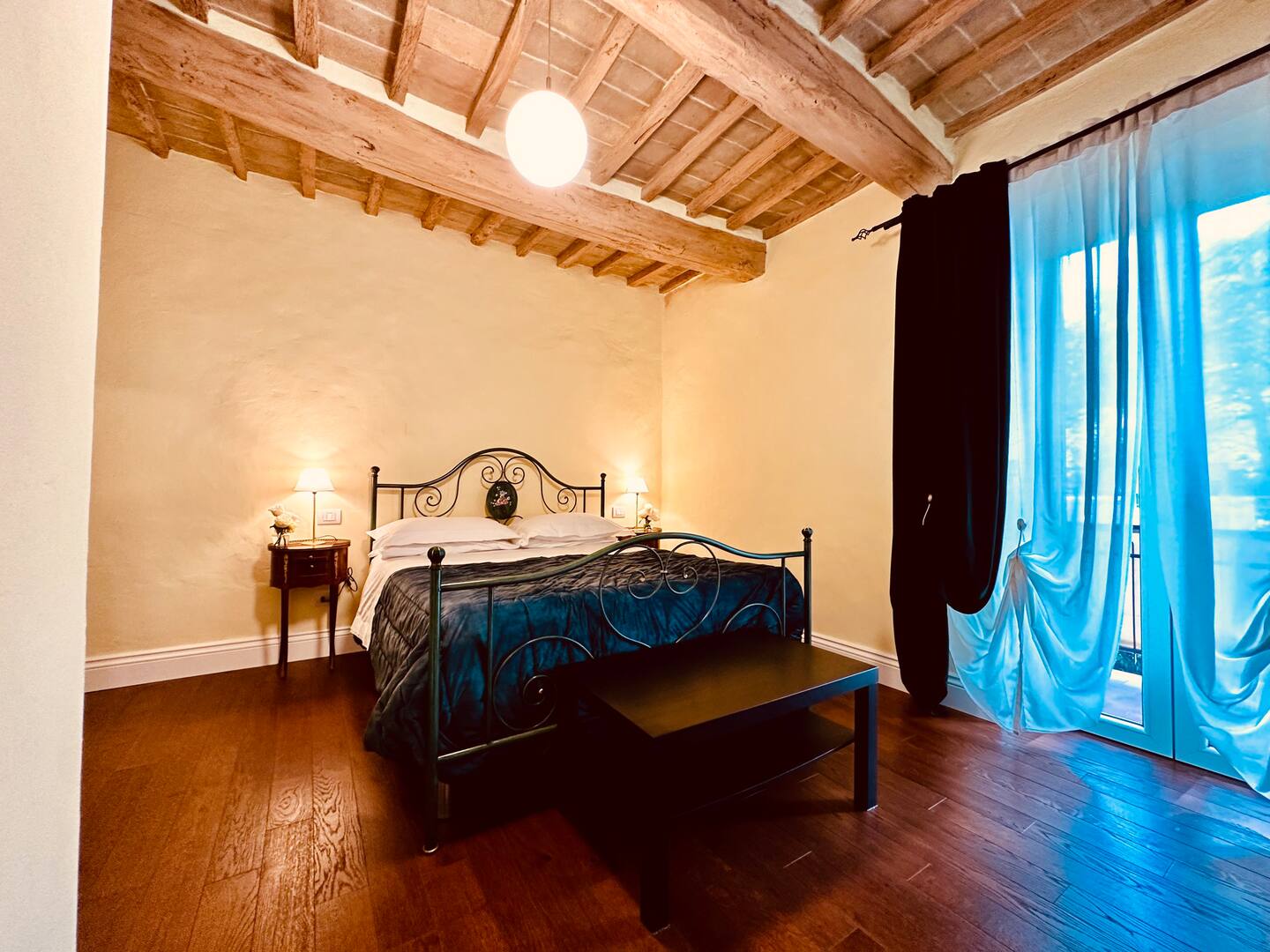 Camera confortevole con letto matrimoniale, stufa e accesso a un piccolo terrazzo. Atmosfera semplice e rilassata.