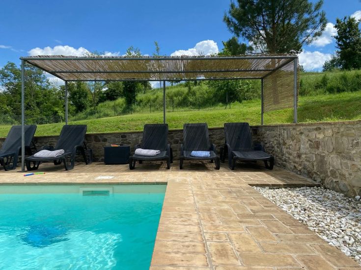 Une zone de détente avec des chaises longues près d'une piscine, entourée de plantes vertes et ombragée.