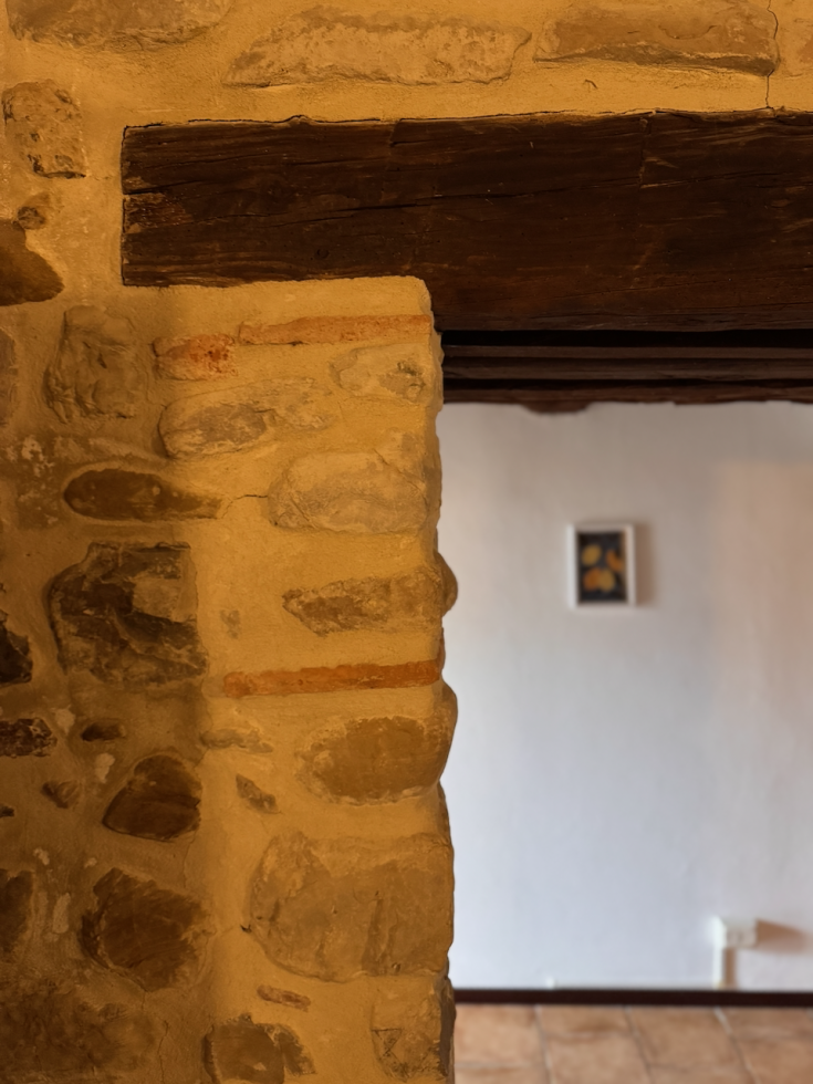 Détail d'un mur en pierre avec une ouverture sur un intérieur rustique. L'espace présente des tons chauds.