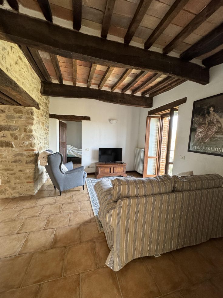 Salon accueillant avec des poutres apparentes et des meubles simples, idéal pour des moments de détente.