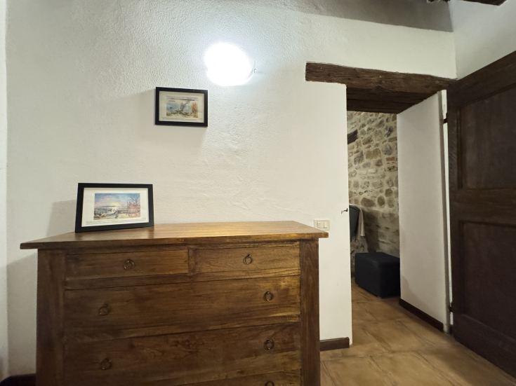 Une pièce simple avec des meubles en bois clair, des œuvres décoratives sur les murs et une porte qui s'ouvre sur un espace traditionnel.