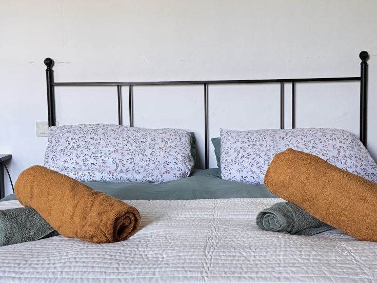 Lit simple avec des serviettes roulées, idéal pour un séjour confortable.