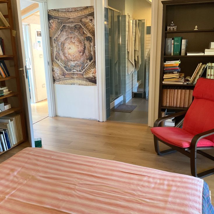 Einfaches Zimmerinterieur mit einem Bücherregal, einem roten Sessel und Wanddekorationen.