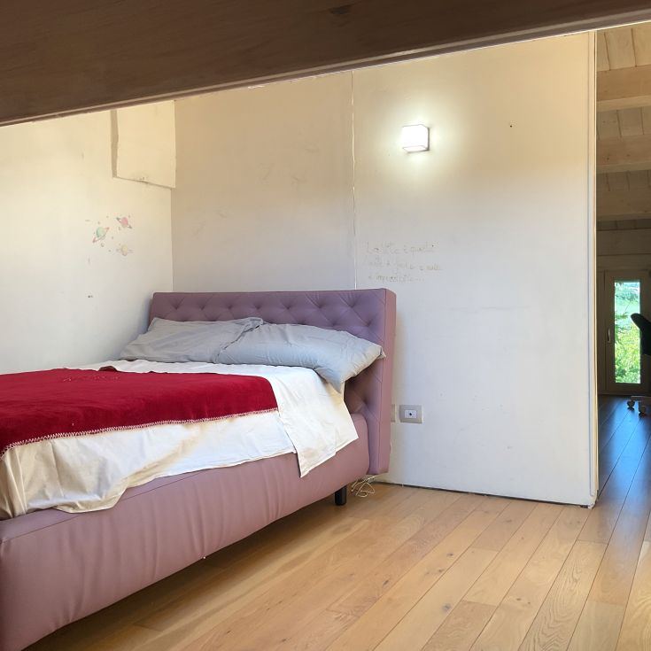 Ein Schlafzimmer mit einem Doppelbett, hellem Holzboden und sanfter Beleuchtung von einer Tischlampe.