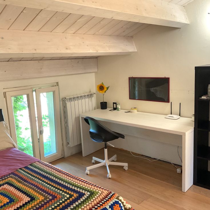 Ein Zimmer mit einem Bett, einem Schreibtisch und einem Fenster, das natürliches Licht hereinlässt.