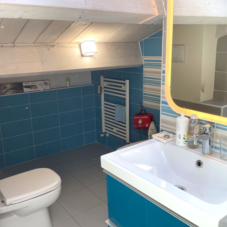 Modernes Bad mit blauen Fliesen und einem großen, beleuchteten Spiegel, ausgestattet mit allen Annehmlichkeiten.