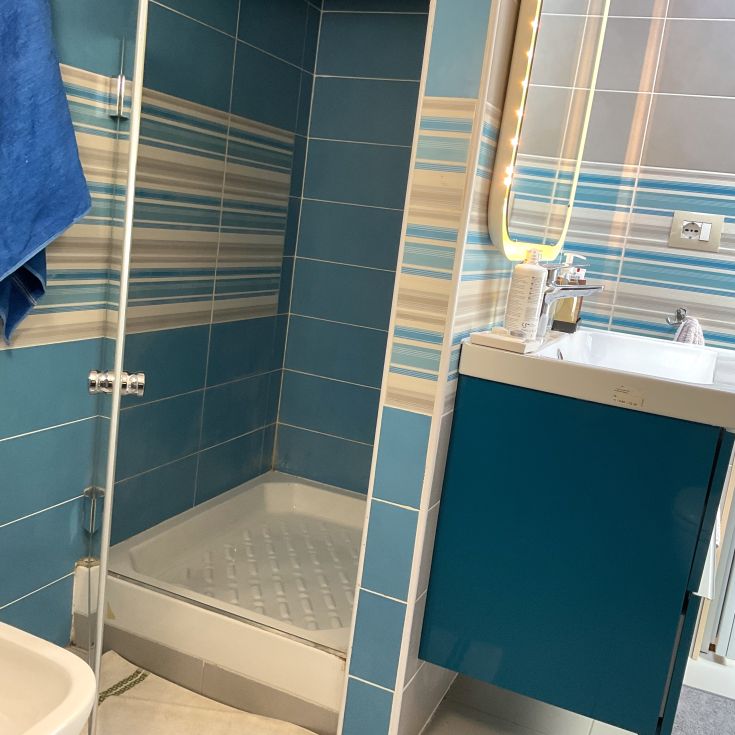 Moderne Badezimmer mit blauen Fliesen und einer Dusche. Enthält ein Waschbecken und einen beleuchteten Spiegel.