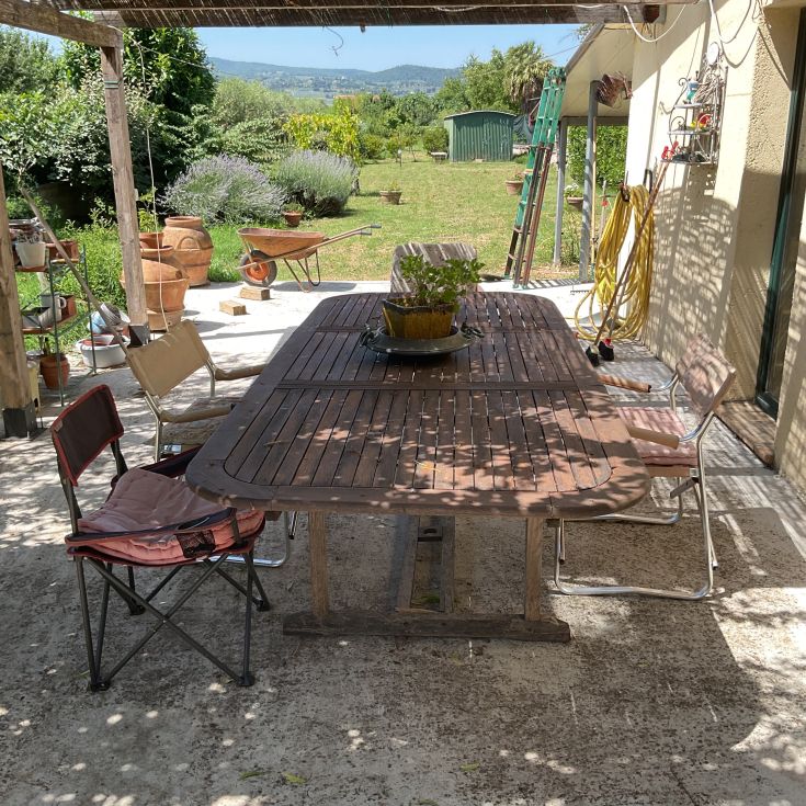Geräumige Veranda mit Schatten, ausgestattet mit einem Tisch und Stühlen, eingebettet in einen ordentlichen Garten.