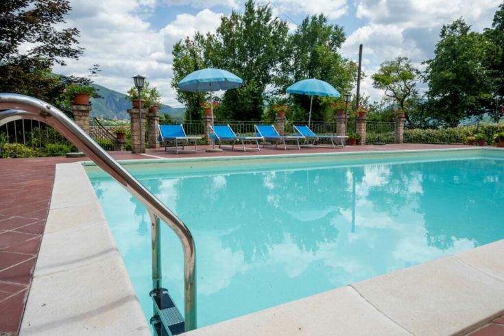 Piscina circondata da alberi e vegetazione, attrezzata con lettini e ombrelloni, perfetta per momenti di relax.