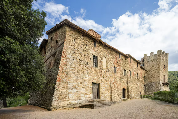 Un antico monastero con torre, circondato da spazi verdi e un cielo sereno.