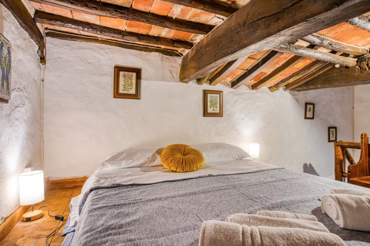 Simple bedroom with wooden beam ceiling, double bed, and neutral-toned decorations.