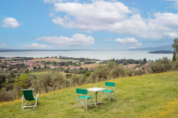 View of Lake Trasimeno with tables and deck chairs on a grassy area.