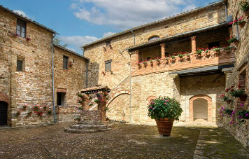 Historical stone courtyard with floral decorations and a central fountain, featuring typical architectural elements.