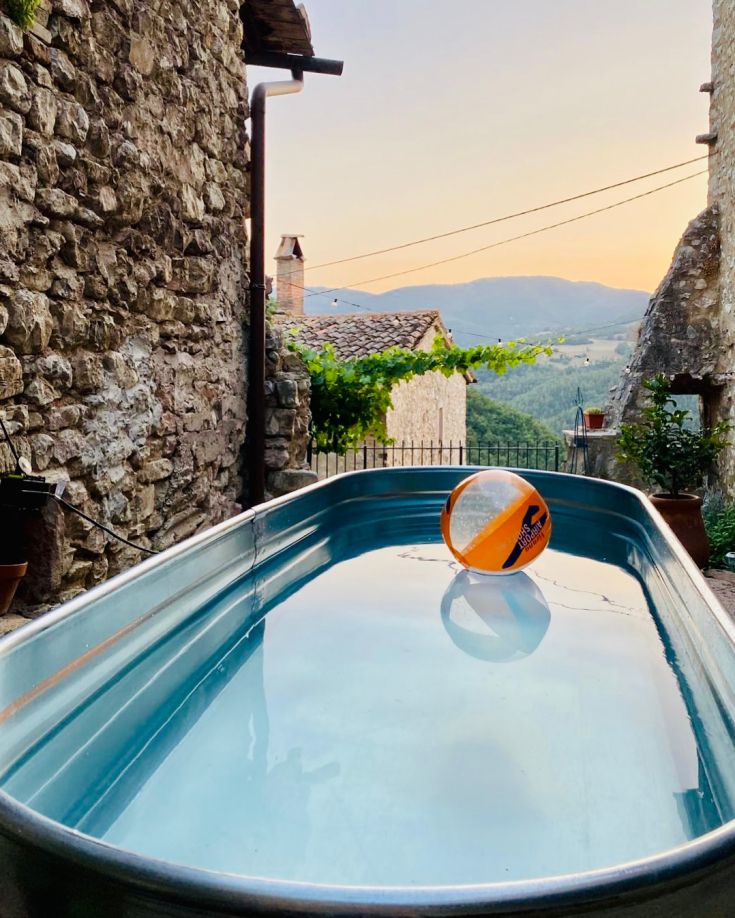 Ein gut gepflegter Pool in einem historischen Dorf, mit einem schwimmenden Ball, der eine sommerliche Atmosphäre hervorruft.