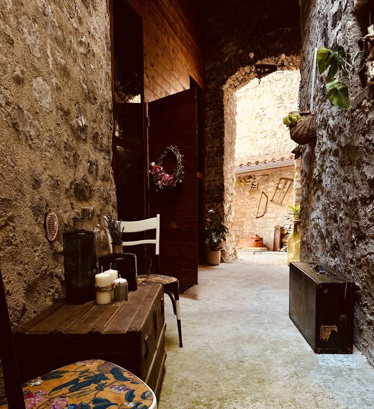 Ein einfacher Korridor aus Stein und Holz, sanft beleuchtet, mit einigen Pflanzen an der Seite, der zu einem Grünbereich führt.