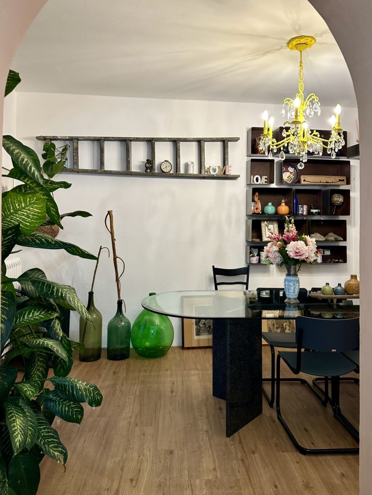 Eine gemütliche Ecke mit einem Glastisch und Vintage-Möbeln, beleuchtet von einem einfachen Kronleuchter.