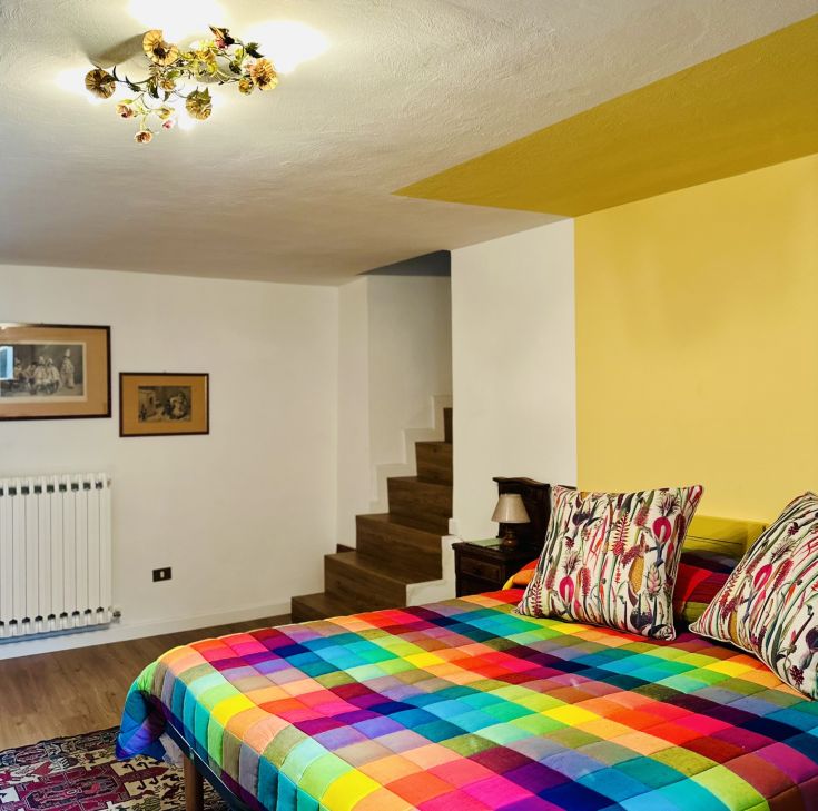 Helle Zimmer mit einem bunten Bett und einfacher Einrichtung, ideal für einen komfortablen Aufenthalt.