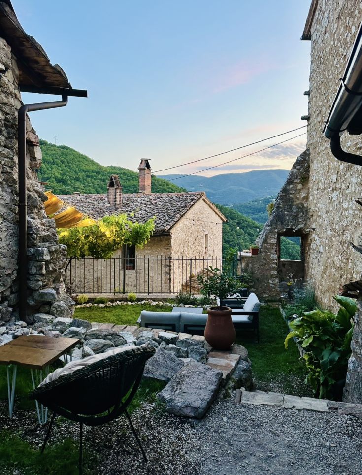 Detail des Dorfes Vallo di Nera, mit Steinbauten, einem gepflegten Garten und den umliegenden grünen Bergen.