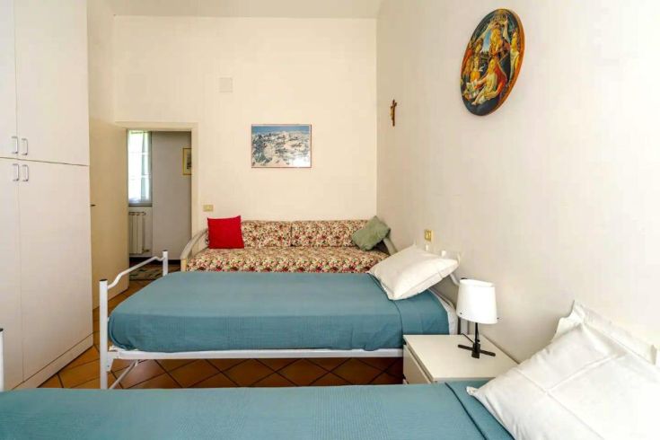 A simple room with single beds and a floral-patterned sofa, bathed in natural light.