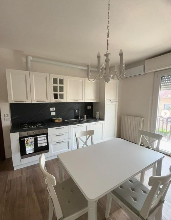 Cucina ben illuminata con arredi moderni, un tavolo bianco ed un lampadario semplice.