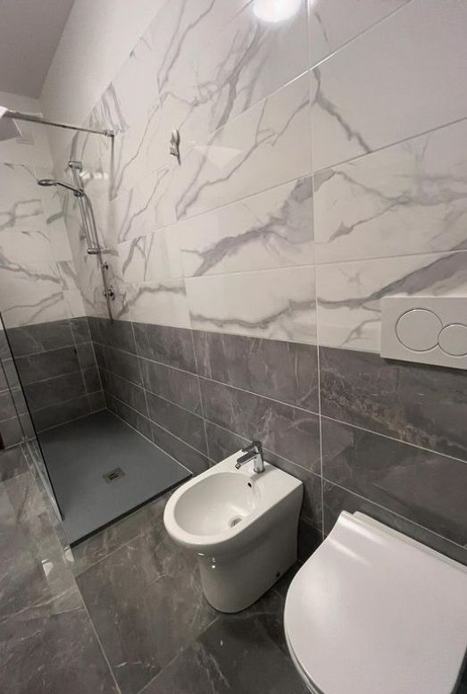 Bagno con piastrelle grigie e bianche, dotato di box doccia e arredamento semplice.