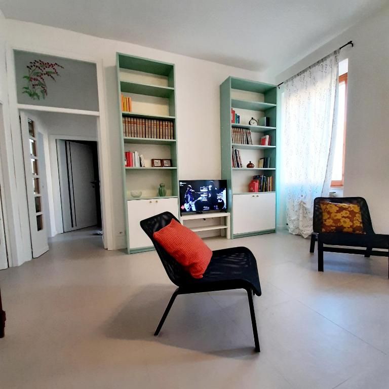 Spacious and bright living room, simply and functionally furnished, featuring a bookshelf and decorative elements.