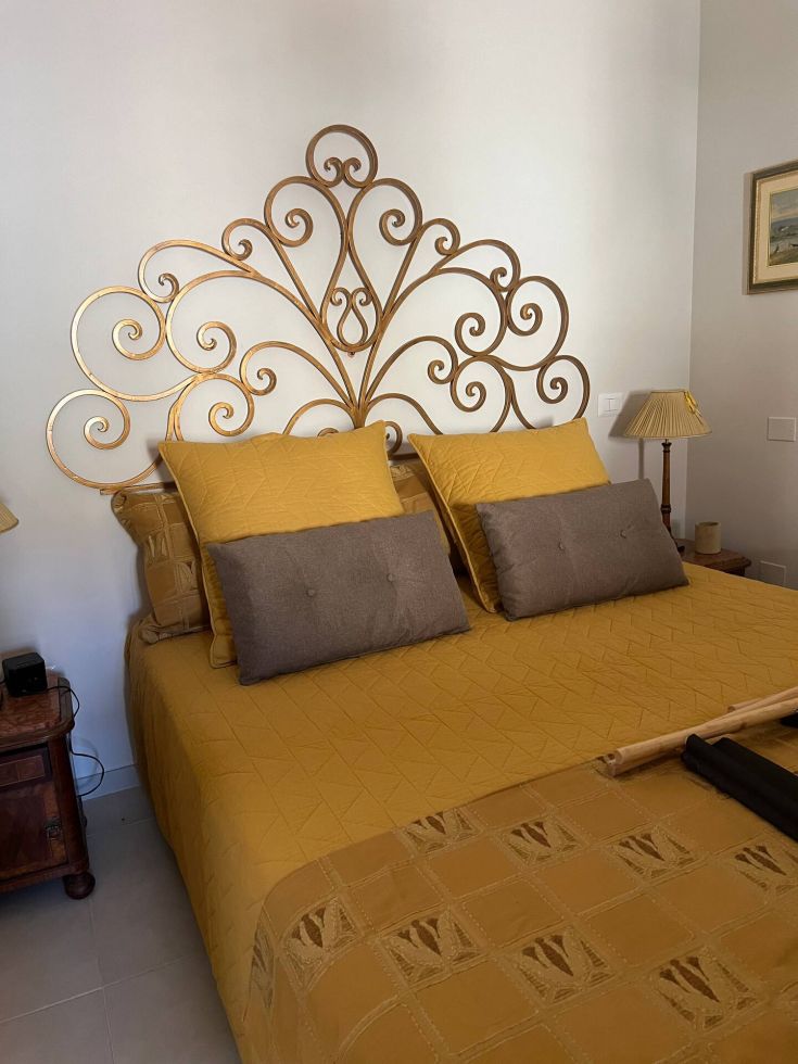 Simple double bedroom with a metal headboard and light yellow bedding. Cozy and relaxing space.