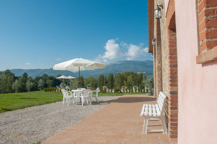 Panorama tranquillo di un agriturismo con tavolini all'aperto, circondato dalla natura e da dolci colline.