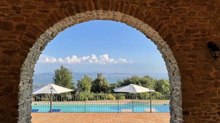 View of the swimming pool and the Umbrian countryside seen through a stone arch.