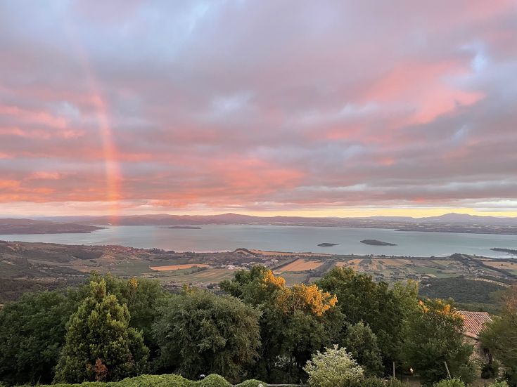 A scene on Lake Trasimeno with a rainbow arching across a colorful sunset sky.