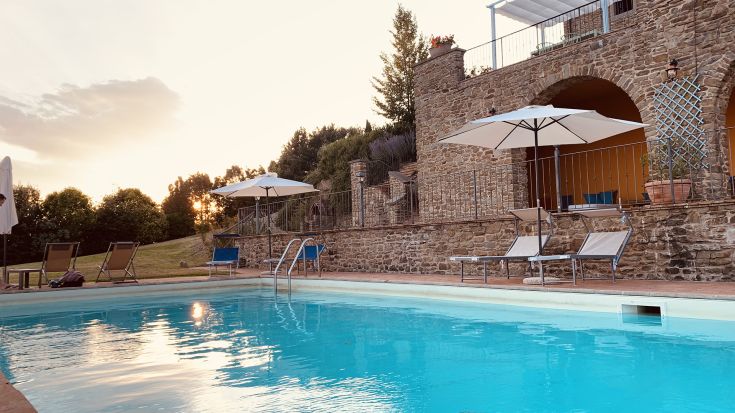 A villa located in Umbria, surrounded by trees and nature, featuring a pool and a view of Lake Trasimeno.