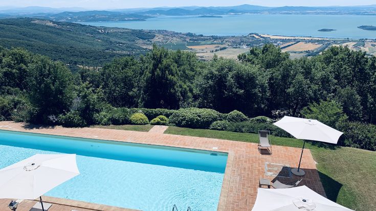 View of Lake Trasimeno from a villa with a pool, surrounded by green spaces.