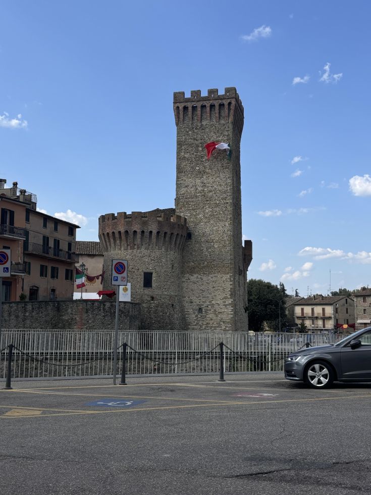 Una torre antica con una bandiera, situata nel centro di un tipico borgo umbro.