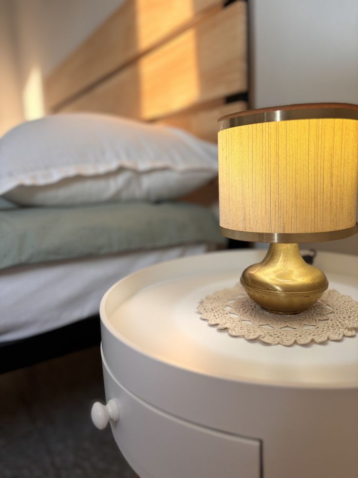 Lampada semplice su un comodino vicino a un letto sistemato, all'interno di una camera accogliente.