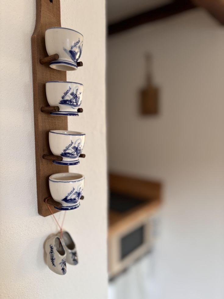 Collezione di tazze appese a una parete, con decorazioni ispirate alla tradizione e zoccoli in ceramica.
