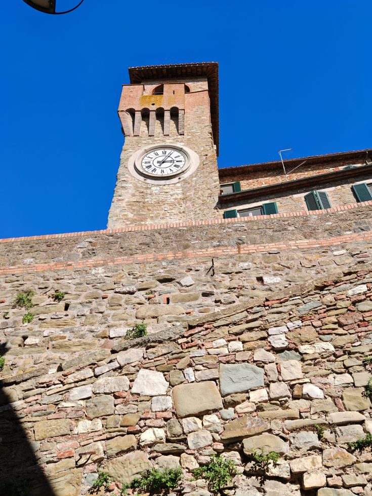 A clock tower stands tall in the medieval village, surrounded by well-preserved stone walls.
