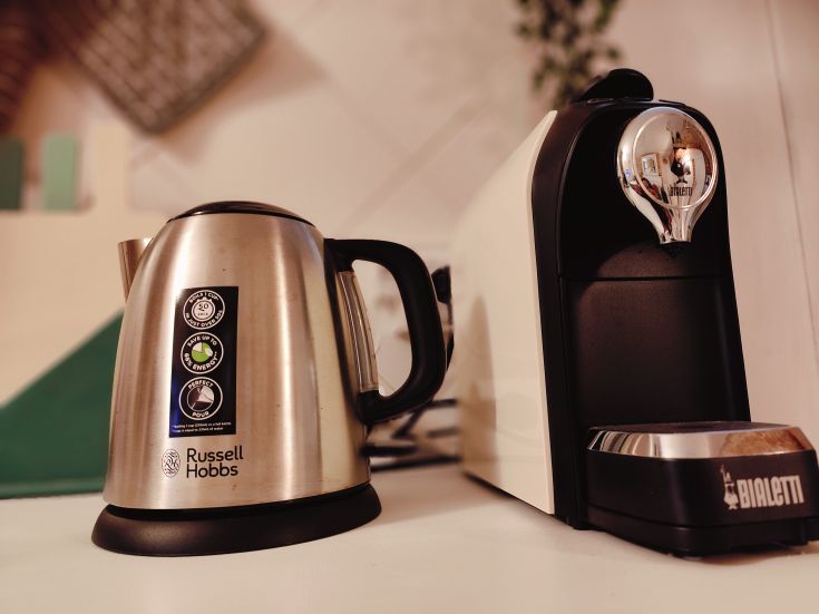 A practical stainless steel kettle next to a coffee machine, both useful in the kitchen.