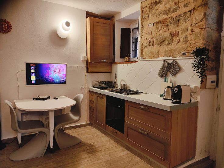A modern and comfortable kitchen with a table and TV screen, featuring wood and stone details.