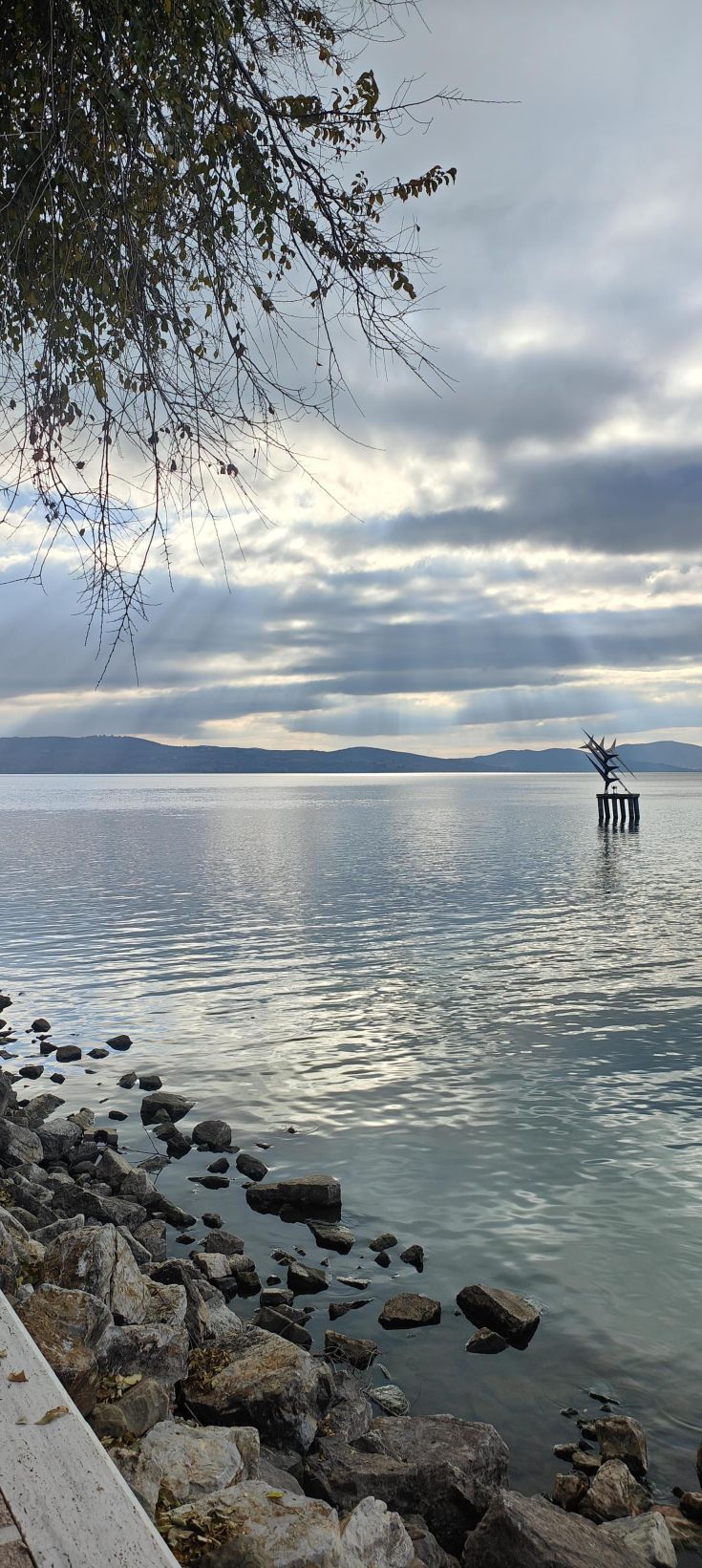 A serene lake view featuring a sculpture at its center, surrounded by clouds in the sky.