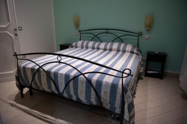 Camera accogliente con letto matrimoniale, decorazioni sobrie e pareti di un verde tenue.