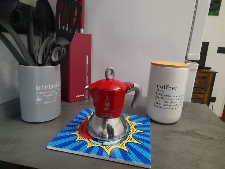 Un moka rouge sur un plan de travail, entouré d'ustensiles de cuisine et d'un bocal de café, simple et fonctionnel.