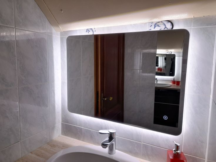 Un miroir moderne éclairé dans une salle de bain contemporaine avec des détails simples et des carreaux clairs.