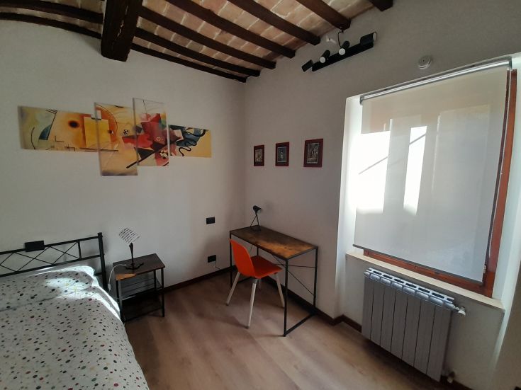 Chambre simple avec un décor épuré, comprenant un bureau et une bonne lumière naturelle.