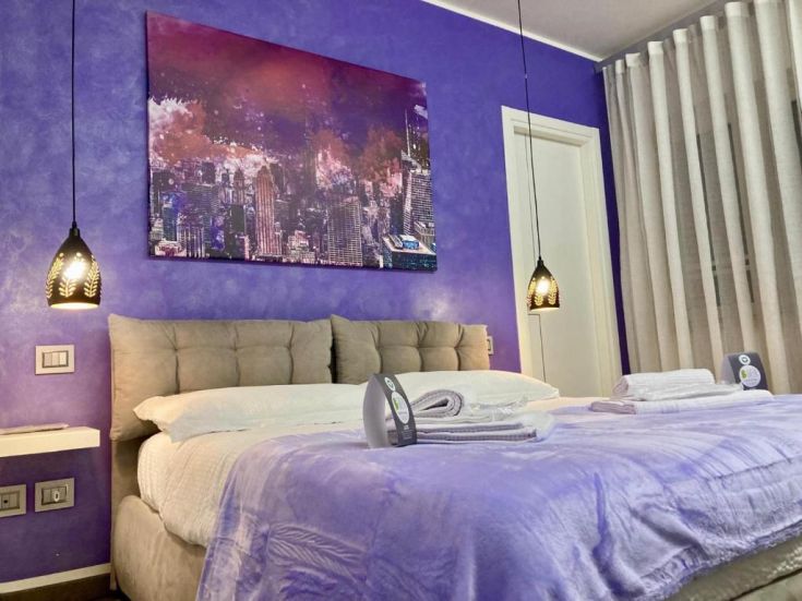 Camera semplice con pareti viola, letti ordinati e decorazioni contemporanee.