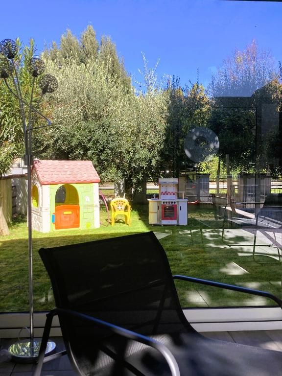 Un giardino privato spazioso con giochi per bambini, circondato da alberi e un cielo azzurro.