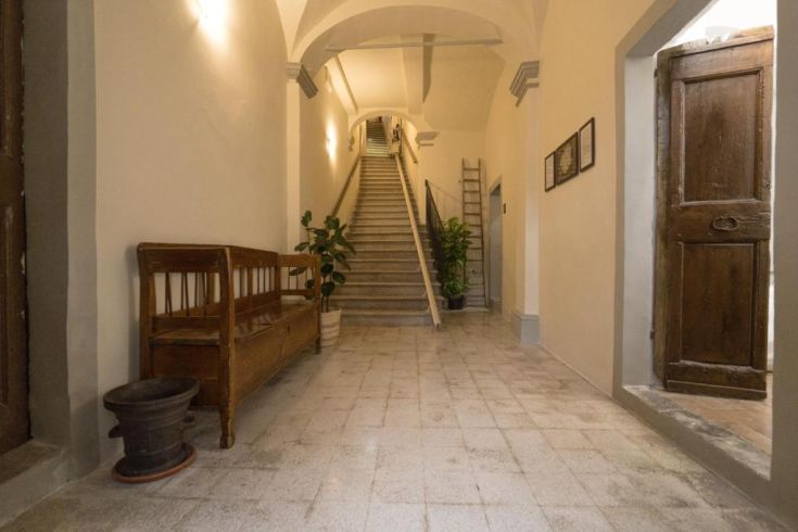 Un couloir menant à un escalier, avec des plantes et des bancs dans un environnement simple et accueillant.