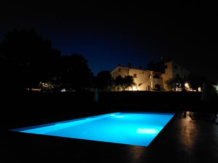 Ein beleuchteter blauer Pool befindet sich in einem Landhaus, umgeben von Natur bei Nacht.