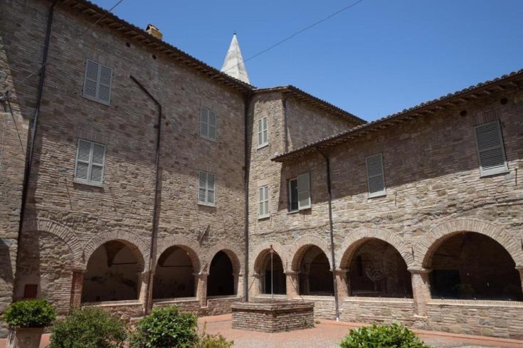 A quiet courtyard with stone arches and historic buildings, located in an Umbrian town.